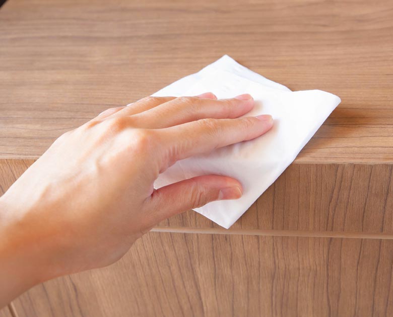 Eine Hand wischt mit einem Putztuch eine Ecke eines Holz-Möbelstückes ab.